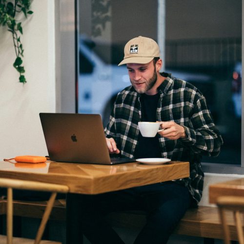 Flannel shirted man with cap, coffee cup and laptop searching for a life coach near me